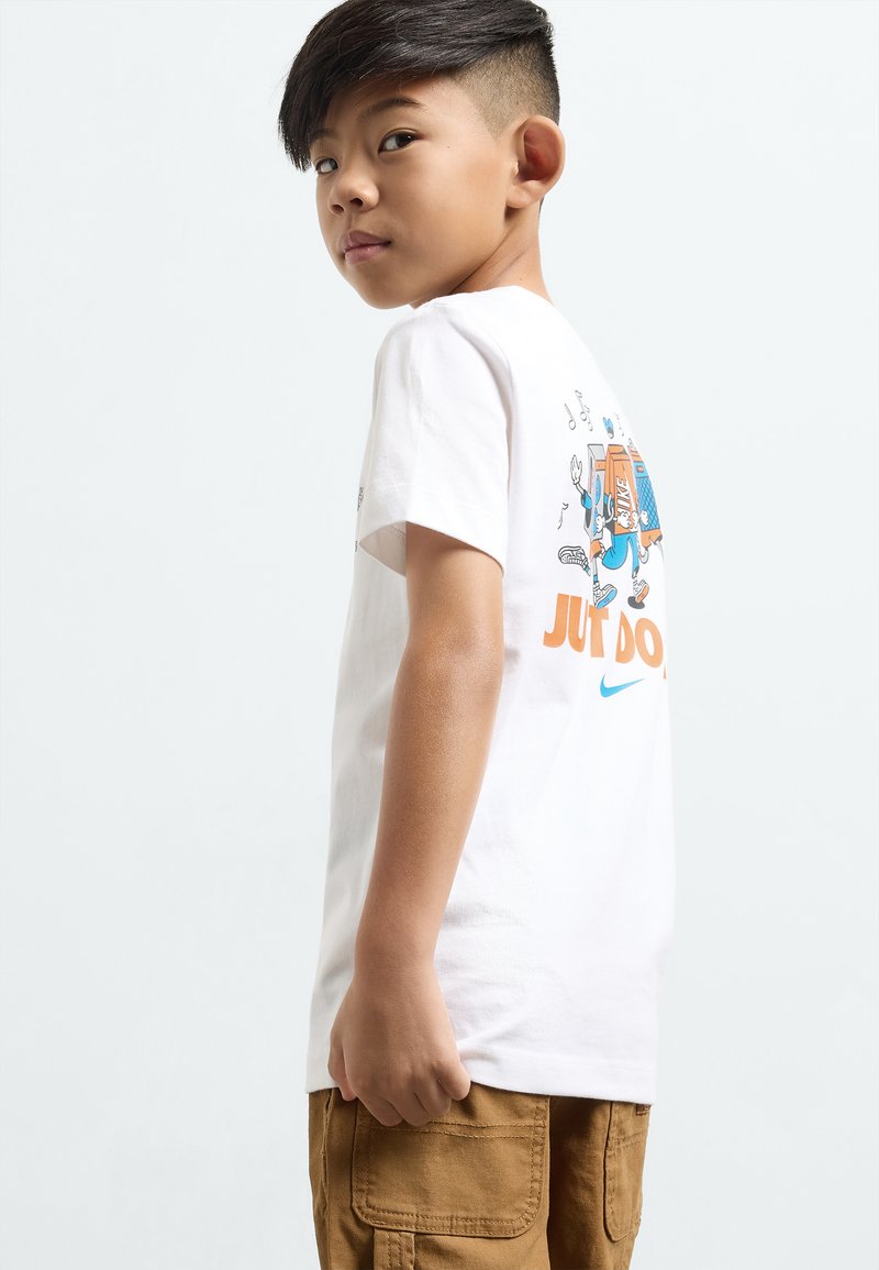 Balts kokvilnas T-krekliņš ar krāsainu grafikā dizainu aizmugurē, uz kura ir teksts "TIKAI DARI TO" un zils Nike logo. Īsas piedurknes.
