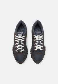 Sneaker grigie e marroni con lacci bianchi, caratterizzate da una tomaia in tessuto testurizzato, colletto imbottito e suola in gomma con battistrada pronunciato.