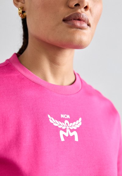 Roosa puuvillane T-särk, mille esitaskus on valge MCM logo ja sümbol, klassikalise ümarakaeluse ja lühikeste varrukatega.