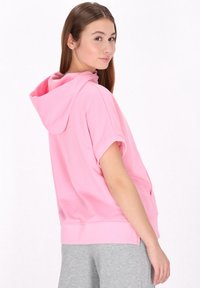 Felpa corta rosa con maniche a sbuffo, tasca frontale e cappuccio regolabile con cordino. Materiale morbido, vestibilità rilassata e rifinita con polsini a costine.