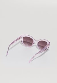 Gafas de sol moradas semitransparentes con lentes degradados, montura redondeada y varillas delgadas con un sutil patrón en el lado exterior.