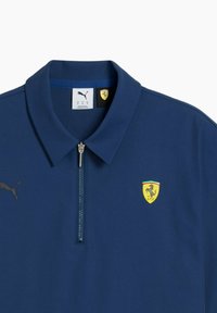 Tricou polo de marină cu guler cu fermoar, logo Puma pe partea stângă și emblemă Ferrari galbenă cu un cal țopăind.