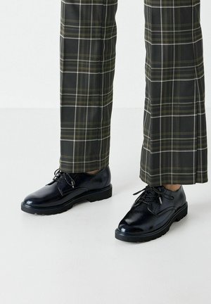 Black, patent leather dress shoes with rounded toes, lace-up design, and textured surface, paired with plaid green and black trousers.