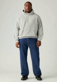 Sweatshirt capuz cinza claro, jeans azuis e sapatos pretos. O sweatshirt tem um bolso canguru; os jeans têm um corte clássico com um leve desgaste.