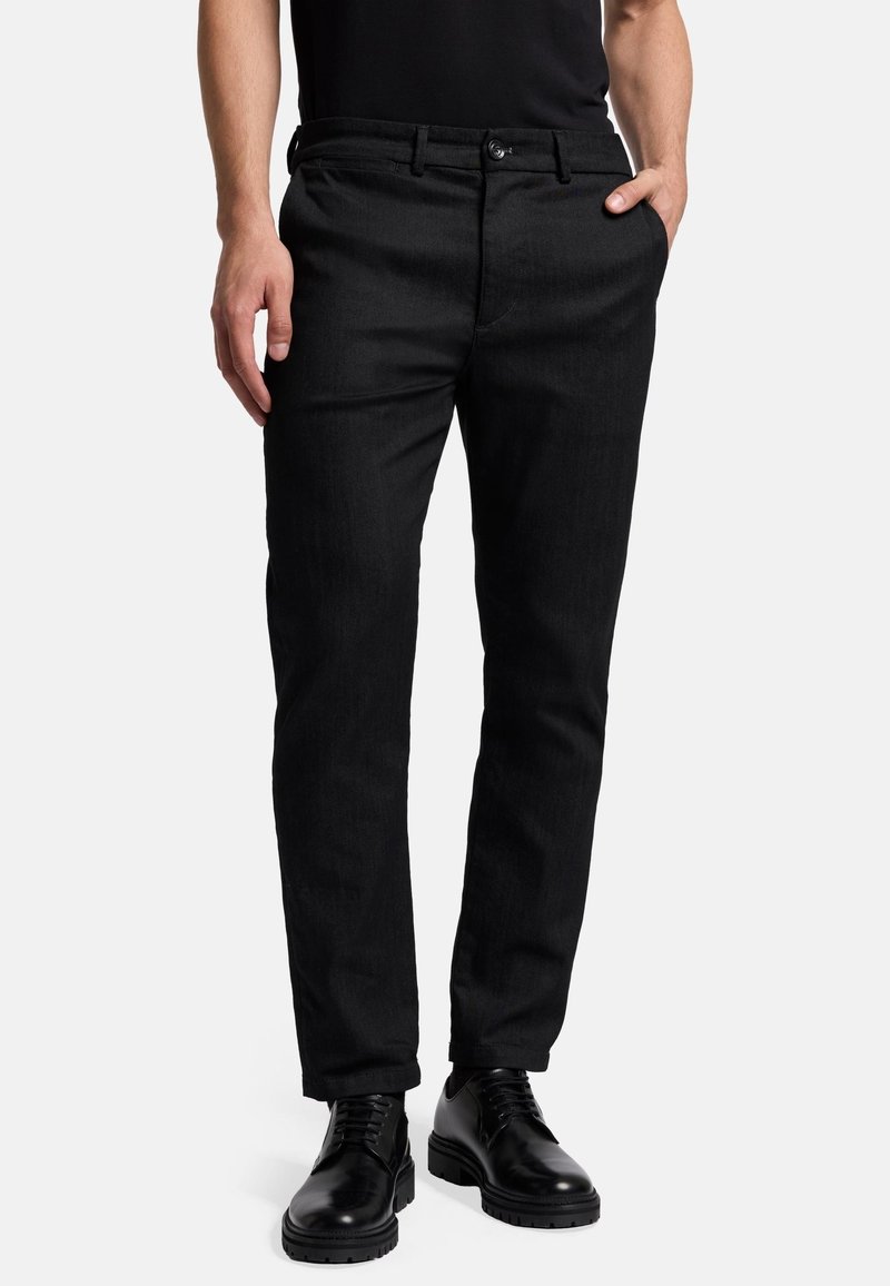 Schwarze Jeanshosen mit schlanker Passform, leicht strukturiertem Stoff, vorderen Taschen und Knopfverschluss, kombiniert mit schwarzem Schuhwerk.