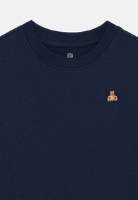 Tengerészkék babapulóver bordázott kerek nyakkivágással és bal oldali mellrészen kis hímzett barna mackóval.