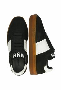 Schwarze Wildledersneaker mit weißen Akzenten, runde Zehenpartie, Gummilaufsohle und schwarzen Schnürsenkeln. Mit einem Logo auf der Zunge und der Seite.