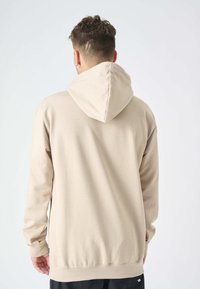 Felpa beige con cappuccio regolabile, maniche lunghe e polsini a costine. Tessuto liscio con cuciture minime e vestibilità rilassata.