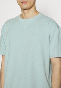 Světle modré bavlněné tričko s krátkým rukávem, volný střih a jemný výstřih do V. Měkká textura a minimální design.