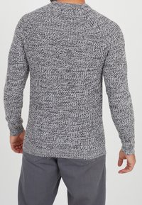 Szary sweter z dzianiny o teksturowanym wzorze, okrągłym dekolcie i długich rękawach. Noszony z szarymi spodniami, prezentując swobodny styl.