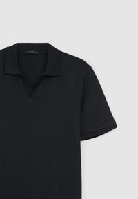 Polo noir à manches courtes avec un motif texturé et un col ouvert sur un fond clair uni.