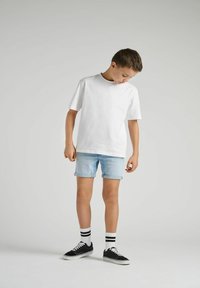 T-shirt en coton blanc à manches courtes, associé à un short en denim bleu clair. Baskets noires avec des chaussettes rayées blanches et noires.