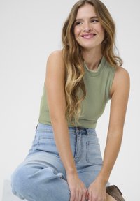Grön ribbad ärmlös topp med hög krage, kombinerad med högmidjade ljusblå denimjeans. Mjuk textur och figurnära design.