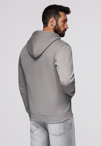 Jasnoszara bluza z kapturem o miękkiej teksturze, z kieszenią kangurzą i ściągaczami, w połączeniu z jasnoszarymi dżinsami.