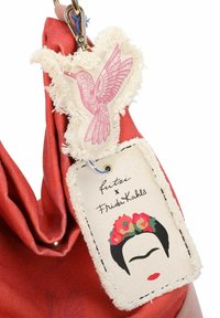 Sac en tissu rouge avec un design froncé. Comprend une étiquette texturée arborant un oiseau rose et une illustration de Frida Kahlo avec des accents floraux.