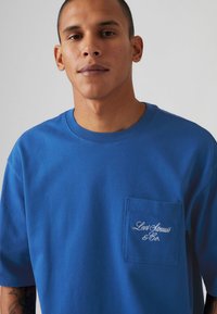 Μπλε βαμβακερό T-shirt με στρογγυλή λαιμόκοψη, κοντά μανίκια και αριστερό τσεπάκι στο στήθος με λευκή κεντημένη επιγραφή "Levi Strauss & Co."