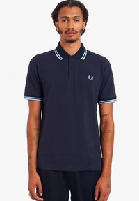 Camiseta polo navy de algodón, con una tapeta de tres botones, un cuello azul claro en contraste y rayas en las mangas, y un pequeño logo en el pecho.