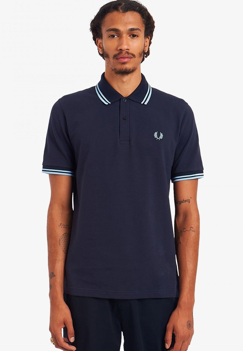 Camiseta polo navy de algodón, con una tapeta de tres botones, un cuello azul claro en contraste y rayas en las mangas, y un pequeño logo en el pecho.