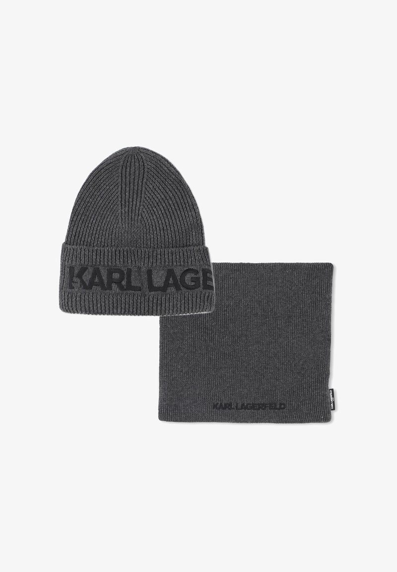 Bonnet en tricot gris et cache-cou assorti. Les deux présentent une texture côtelée et une bande logo sur le bonnet, tandis que le cache-cou a une surface lisse.