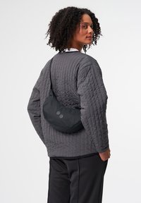 Gep quiltete graue Jacke mit langen Ärmeln, schwarze Umhängetasche mit zwei Knopfakzenten, getragen über schwarzen Hosen. Glatte Textur, modernes Design.