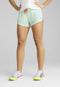 Shorts de sport vert clair avec une taille élastique et un cordon de serrage rouge, dotés d'un tissu texturé et de fentes latérales pour plus de mobilité.