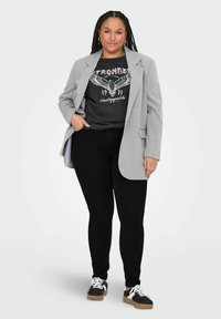 Grå kavaj med ränder över en svart grafisk t-shirt med ett örnmotiv. Bärs med svarta slim fit-jeans och svarta sneakers.