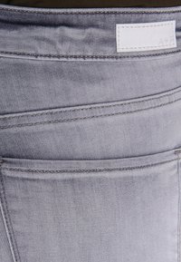 Jeans de mezclilla gris con una textura suave, costura doble a lo largo de la cintura y una etiqueta blanca de la marca cosida en el bolsillo trasero.