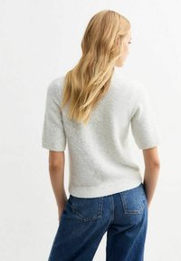 Ljusgrå kortärmad tröja med en strukturerad, mjuk tyg, kombinerad med blå denimjeans. Tröjan har en rundad halsringning och en figurnära nederdel.