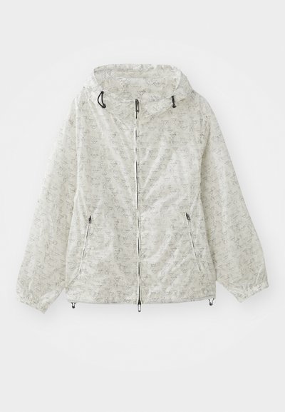 Kerge, kreemjas värvitoonis spordijakk, millel on kapuuts, elastsed varrukaotsad ja korduv geomeetriline muster. Kaks esipakki on kaasas.