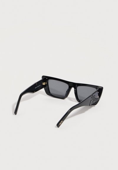 Μαύρα ορθογώνια γυαλιά ηλίου με σκούρους φακούς, παχιά πλαίσια και χρυσή επιγραφή "MCM" στο μπράτσο, καθώς και ανάγλυφο λογότυπο στο πλάι.