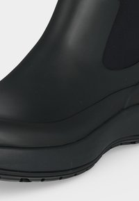 Gros plan d'une botte d'anxi noire en caoutchouc avec une semelle épaisse et un panneau latéral élastique.