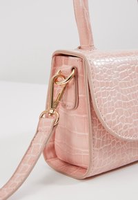 Borsa a tracolla rosa chiaro con texture a coccodrillo, accessori in oro e tracolla removibile. Presenta una forma strutturata e rifiniture lisce.
