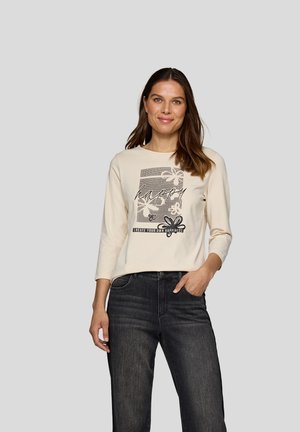 Cremfarbene Langarm-T-Shirt mit einem grafischen Design, das Blumen und das Wort "happy" umfasst. Kombiniert mit dunkelblauen Denim-Jeans.