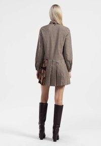 Abito a camicia a scacchi con maniche lunghe, gonna plissettata, pannello a motivo contrastante sul lato e stivali marroni fino al ginocchio.