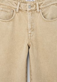 Beżowe dżinsy z denimem o fakturowanym wykończeniu, z przodem zapinanym na guzik i zamek błyskawiczny, szlufkami na pasek oraz dwiema przednimi kieszeniami.