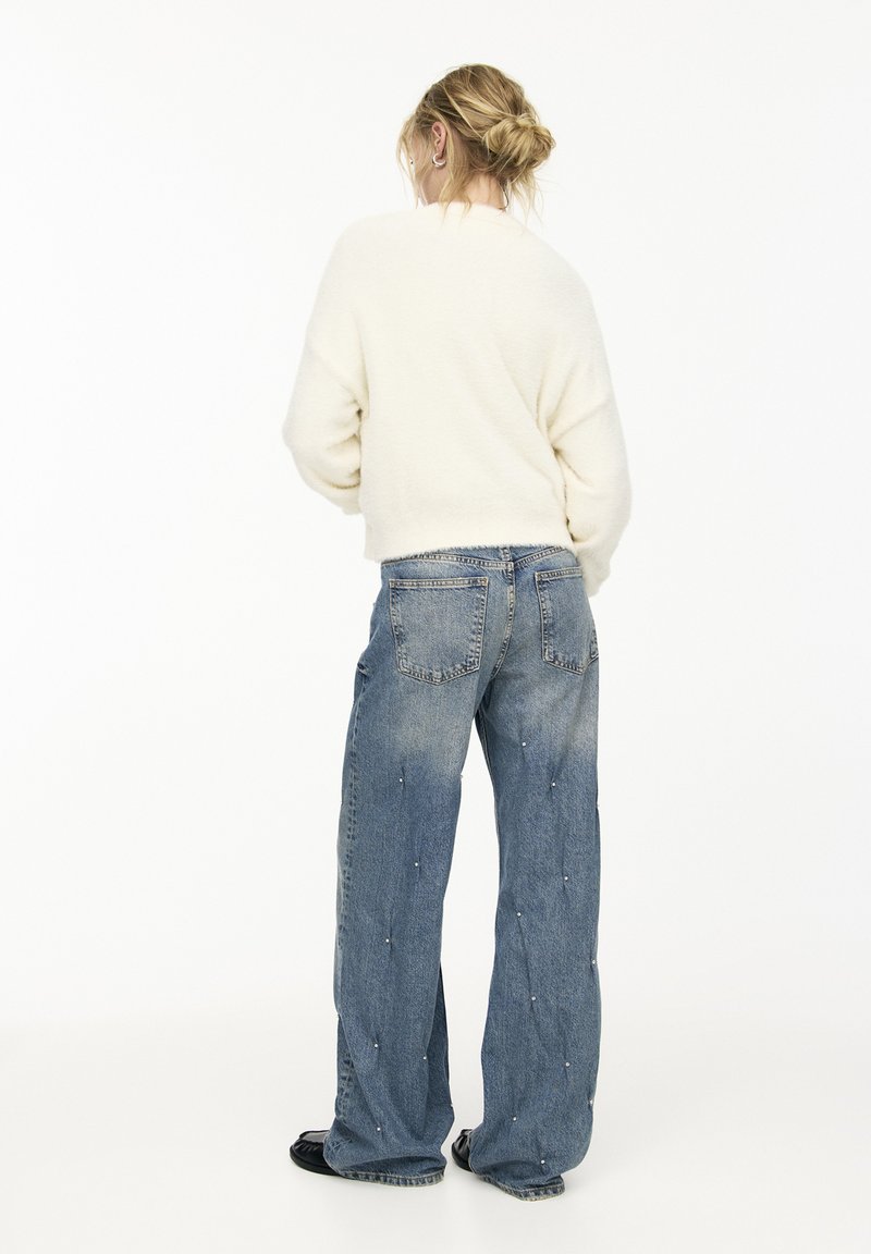 Pull en crème, duveteux, associé à un jean large bleu clair avec des embellissements éparpillés et un délavage usé.