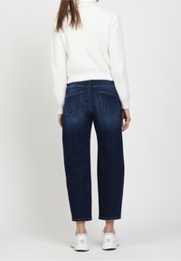 Donkerblauwe high-waisted jeans met een losse pasvorm en achterkantzakken, gecombineerd met een witte, gestructureerde trui en witte sneakers.