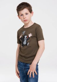 Camiseta de algodón marrón con un gráfico de un topo de dibujos animados sosteniendo una pequeña pala. Mangas cortas, cuello redondo y corte relajado. Combinada con jeans azules.