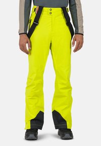 Pantaloni da sci impermeabili gialli con dettagli neri, spallacci regolabili e chiusura frontale con bottone. Presenta più tasche e una vestibilità ampia.