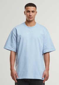 Svijetloplava oversized majica od pamuka s kratkim rukavima i okruglim izrezom. Sadrži mali bijeli ispisani logotip na prsima.