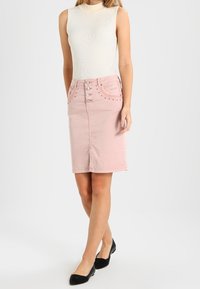 Ljusrosa denim blyertskjol med dekorativa knappar och subtila detaljer; parat med en figurnära vit ribbad ärmlös topp och svarta lägenheter.