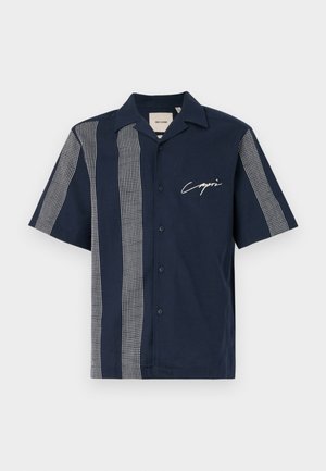 Short-sleeve navy shirt made of cotton with white grid-pattern stripes and "Capri" branding on the chest. Button-up design.