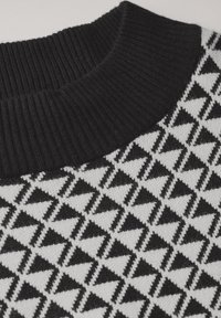 Maglione lavorato a maglia in bianco e nero con colletto a coste, caratterizzato da un motivo geometrico di triangoli su uno sfondo chiaro.