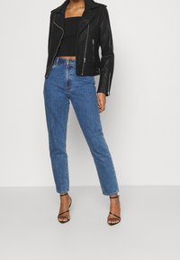 Veste en cuir noir de style biker cropped, jeans taille haute bleus et talons aiguilles noirs avec lanières. Ajustement moderne avec des détails en zip et une coupe droite.