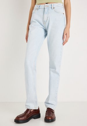 Világoskék, egyenes szárú farmernadrág, magas derékkal, látható varrással és elülső zsebekkel, barna cipővel párosítva.