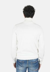 Maglione a collo alto bianco a coste, design aderente, maniche lunghe, indossato con jeans blu, trama semplice, dettagli minimi, visto da dietro.