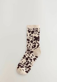 Čarapa boje kreme s rebrastim rubom, koja sadrži tamnosmeđu leopard uzorak. Izrađena je od mekanog, teksturiranog pletenog materijala.