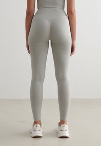 Šedé legíny vyrobené z elastického materiálu, těsně přiléhající design, vysoký pás, hladká textura, doplněné o bílé sportovní boty.