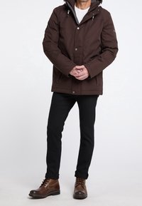 Brown waterproof jacket with a hood, zip front, and snap buttons; paired with black jeans and brown lace-up boots.