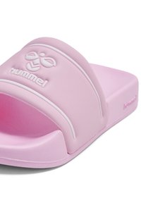 Różowa gumowa sandałka typu klapki z szerokim paskiem ozdobionym białym wytłoczonym logo. Podeszwa jest płaska i teksturowana, co zapewnia przyczepność.